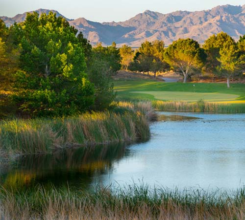 Image of lake in foreground with course hole and mountains in background.